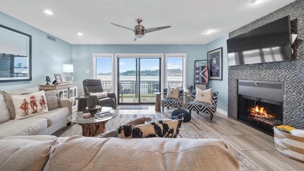 A spacious living room with a fireplace, a ceiling fan, and a large window offering a view of the outdoors. - Updated 2 Bed 2 Bath Condo on beautiful Lake Hamilton 7 minutes from Oaklawn!! (Lake Hamilton)