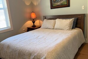 A neatly made bed with a white bedspread and two pillows, a bedside lamp, and a framed picture on the wall. - Small Cozy home just down the road from downtown Guntersville! (Guntersville)