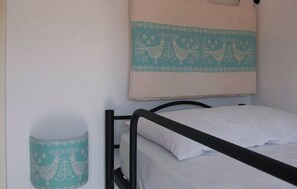 A single bed with a white mattress and pillow, a black metal frame, and a teal wall hanging with peacock designs.