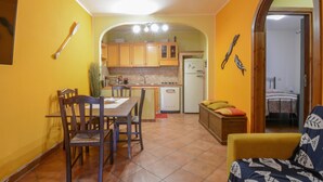 Une cuisine compacte avec des meubles en bois, un réfrigérateur blanc et un coin repas comprenant une table et des chaises.