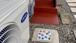 Een gebouw met een rode trap die naar een balkon leidt, een witte airconditioningunit met het label 'Carrier' aan de linkerkant, en een verhard gebied met staptegels.