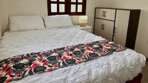 Een slaapkamer met een bed, nachtkastje met lamp, kledingkast en raam met jaloezieën.