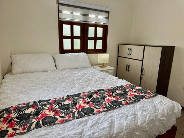 Une chambre à coucher comprenant un lit, une table de chevet avec une lampe, une armoire et une fenêtre avec des stores.