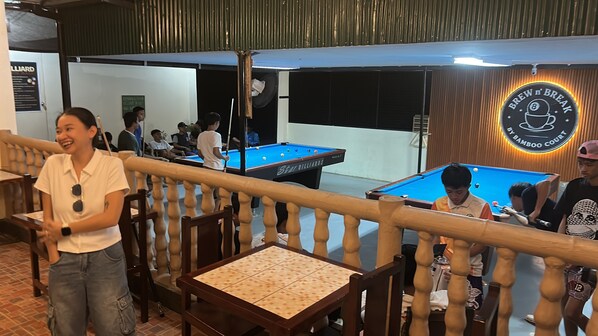 Een biljartzaal met pooltafels, houten leuningen en een bord met de tekst 'Brew n' Break'.