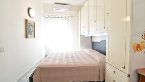 Quarto com cama, guarda-roupa, um quadro na parede e janela com cortinas.