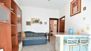 Uma sala de estar com sofá, um armário de madeira e uma área de cozinha com um banquinho.