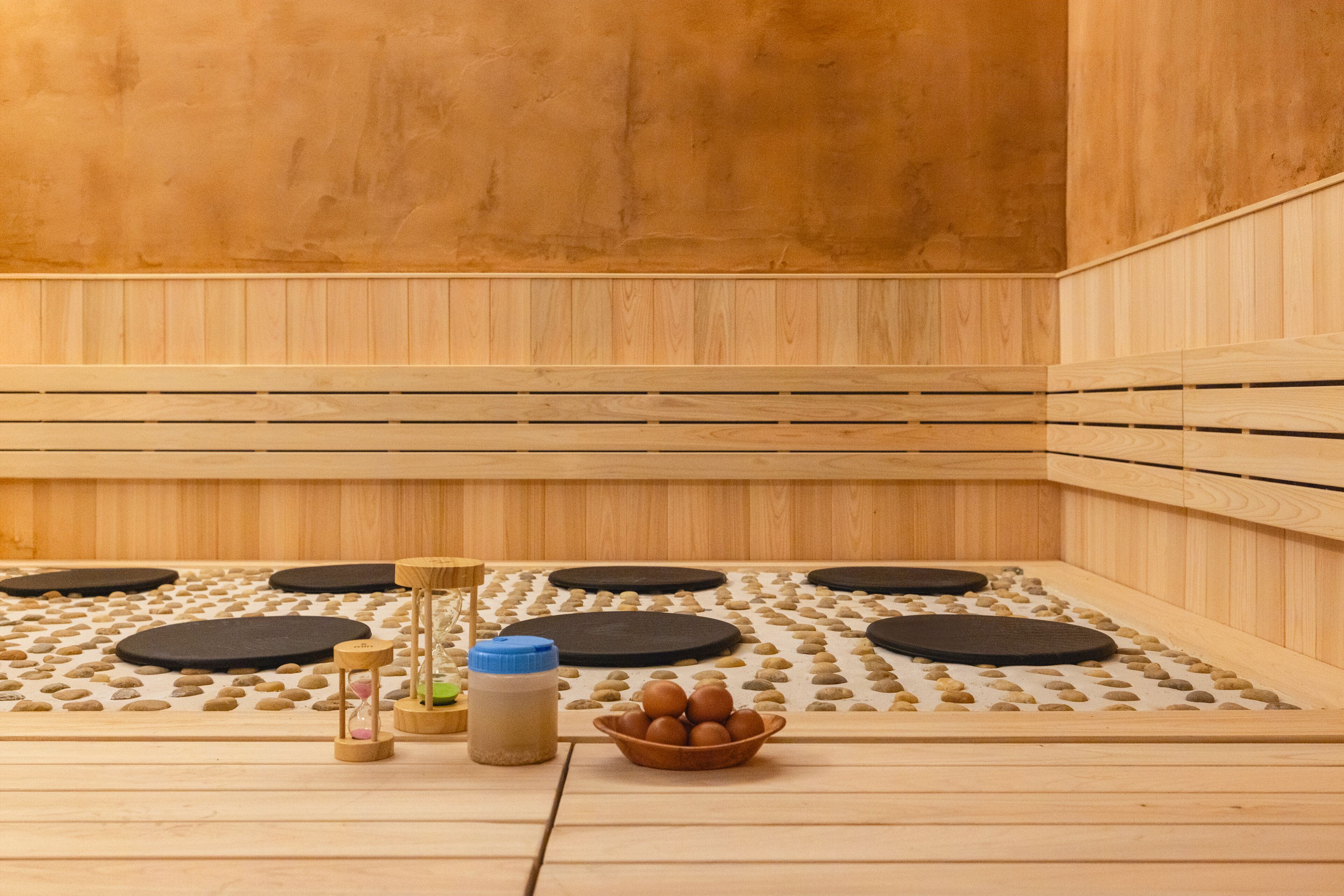 A sauna room with wooden benches, a bowl of brown stones, and two bottles.