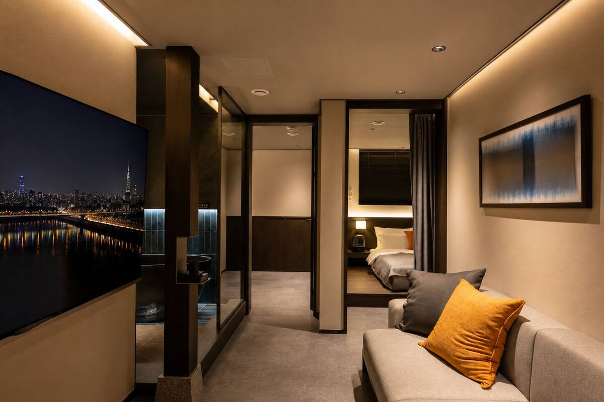 A hotel room with a bed, a sofa, a TV, and a painting.