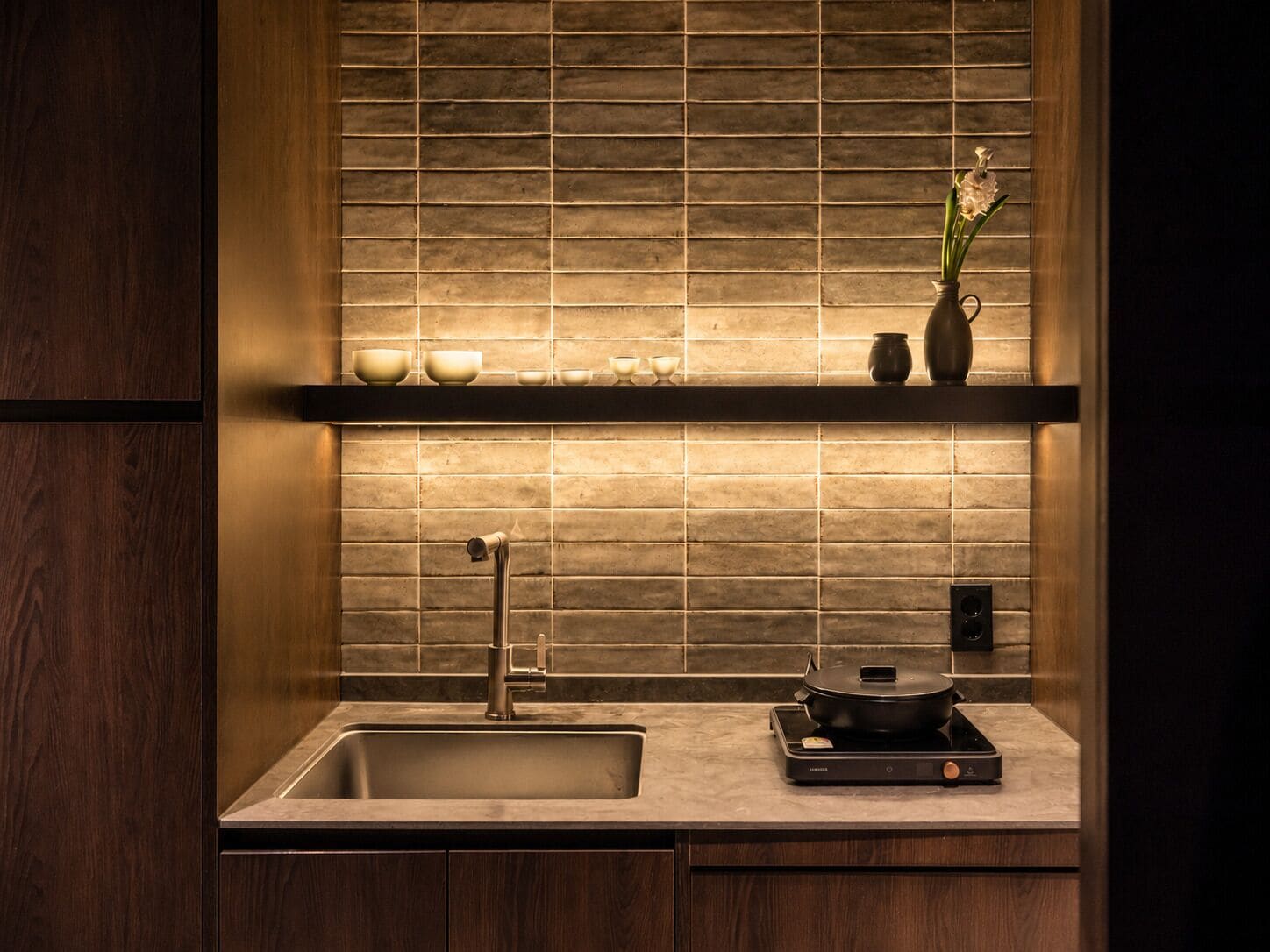 A modern kitchen with a built-in sink, a black induction cooktop, and a shelf with decorative items.