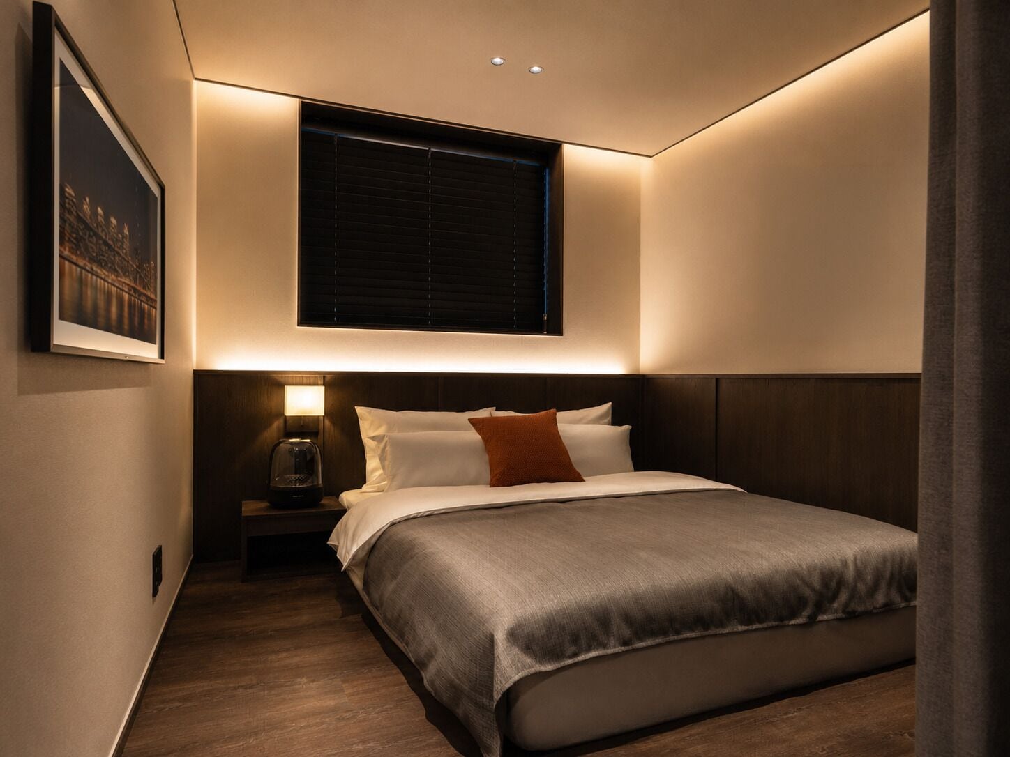 Un dormitorio con cama, mesita de noche, lámpara y ventana con persianas.