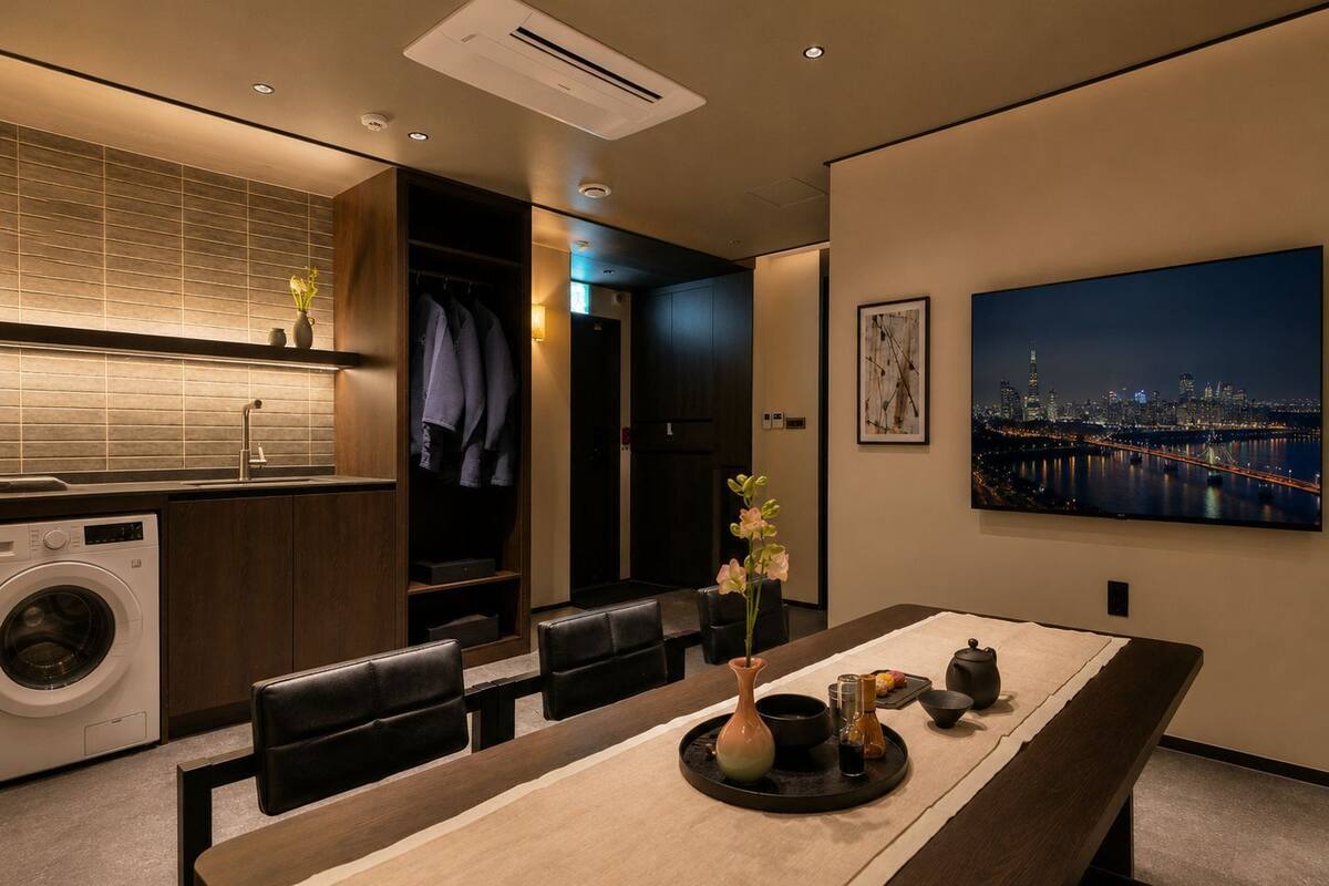 A modern hotel room with a dining area, a washing machine, and a cityscape view.