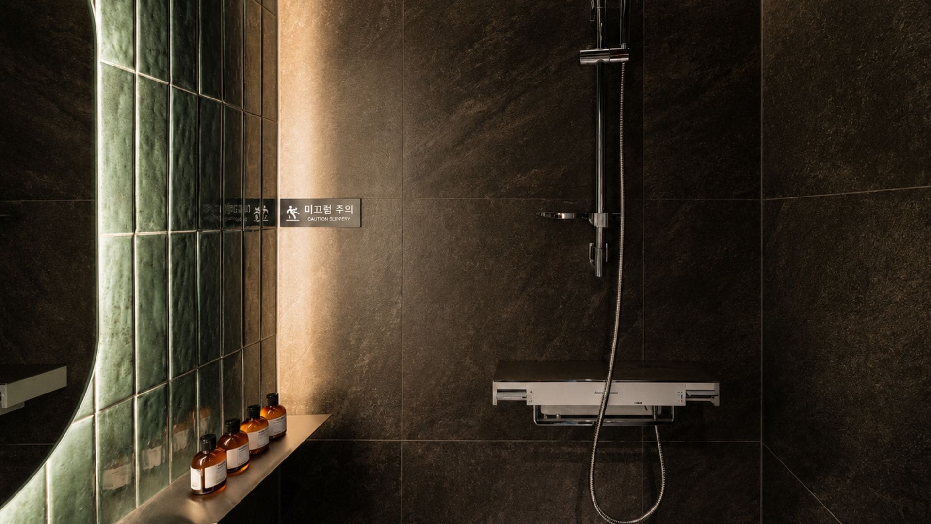 A modern bathroom with a shower, a bench with bottles, and a caution sign.