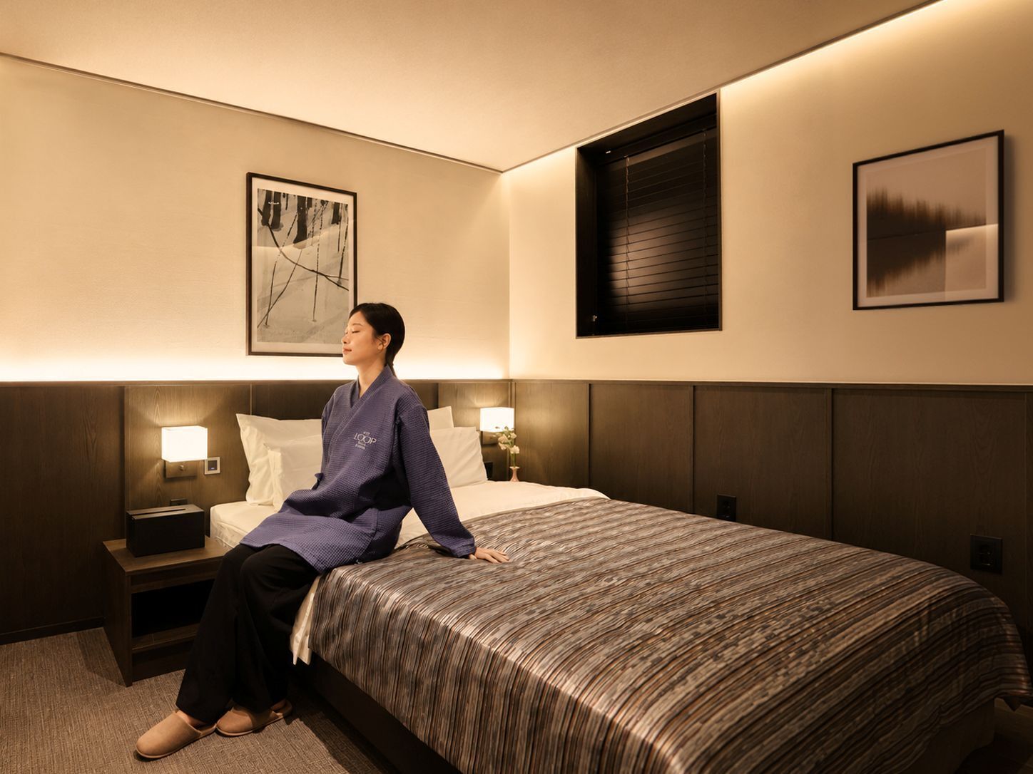 Habitación de hotel con cama, dos lámparas de noche, una mesita de noche, un cuadro en la pared y una ventana con persianas.