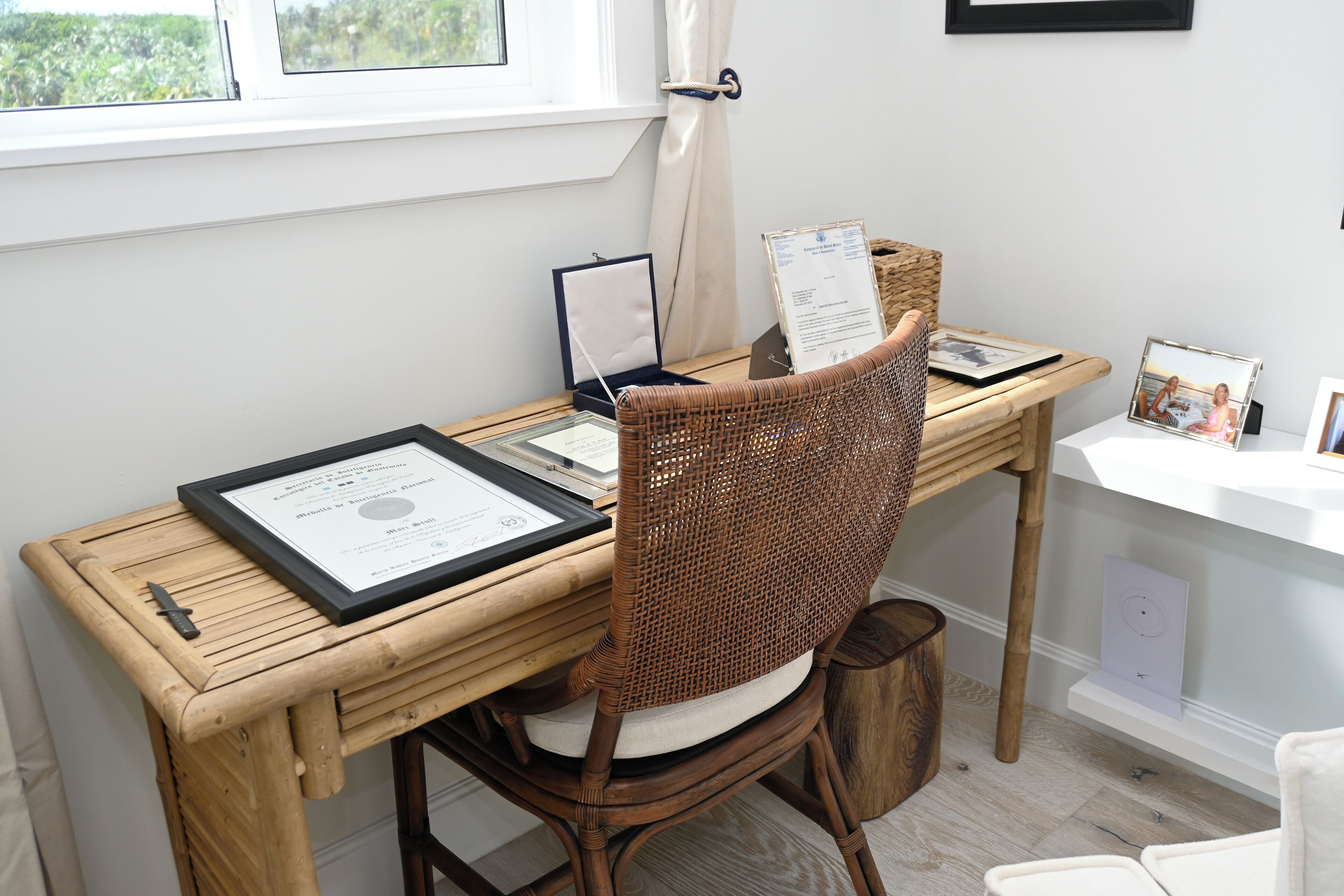 A workspace with a wooden desk, a wicker chair, and a framed certificate.