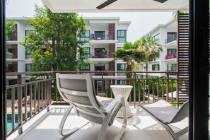 Un balcone con due poltrone e un tavolino, con vista su una piscina e un edificio a più piani con balconi.