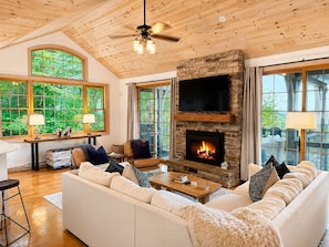 A cozy living room with a fireplace, large windows, and a ceiling fan. - Amazing Sunset View, 1 Mile To Ski & Golf, Sauna, Hot Tub, Wi-Fi, Game Room (Beech Mountain)