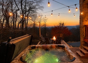 A hot tub with chairs, a fire pit, and string lights against a sunset backdrop. - 5,000ft View, 1 Mile To Ski Resort, Sauna, Hot Tub, Game Room (Beech Mountain)