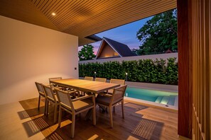 A dining area with a wooden table and chairs, a pool, and a view of a house with a sloped roof. - Tiwa Pool Villa Baan Bua 3 mins to Nai Harn Beach (Rawai)