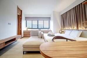 A modern hotel room with a large bed, a sofa, a wooden table, and a view of the outdoors through a large window. - Tiwa Pool Villa Baan Bua 3 mins to Nai Harn Beach (Rawai)