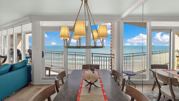 Uma sala de jantar com vista para o oceano, um candelabro e uma mesa com um arranjo decorativo.