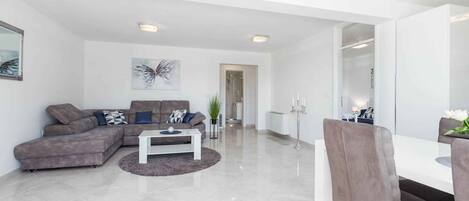 A modern living room with a sectional sofa, a coffee table, and a dining area with a white table and chairs.