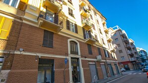 Un immeuble à plusieurs étages avec un commerce au rez-de-chaussée, une entrée bien visible et un ciel bleu dégagé.