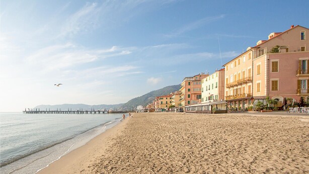Une plage bordée de bâtiments, une jetée qui s’avance dans l’eau et un ciel dégagé.