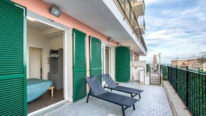 Un balcon avec deux fauteuils de relaxation noirs, des volets verts et une vue sur la ville.