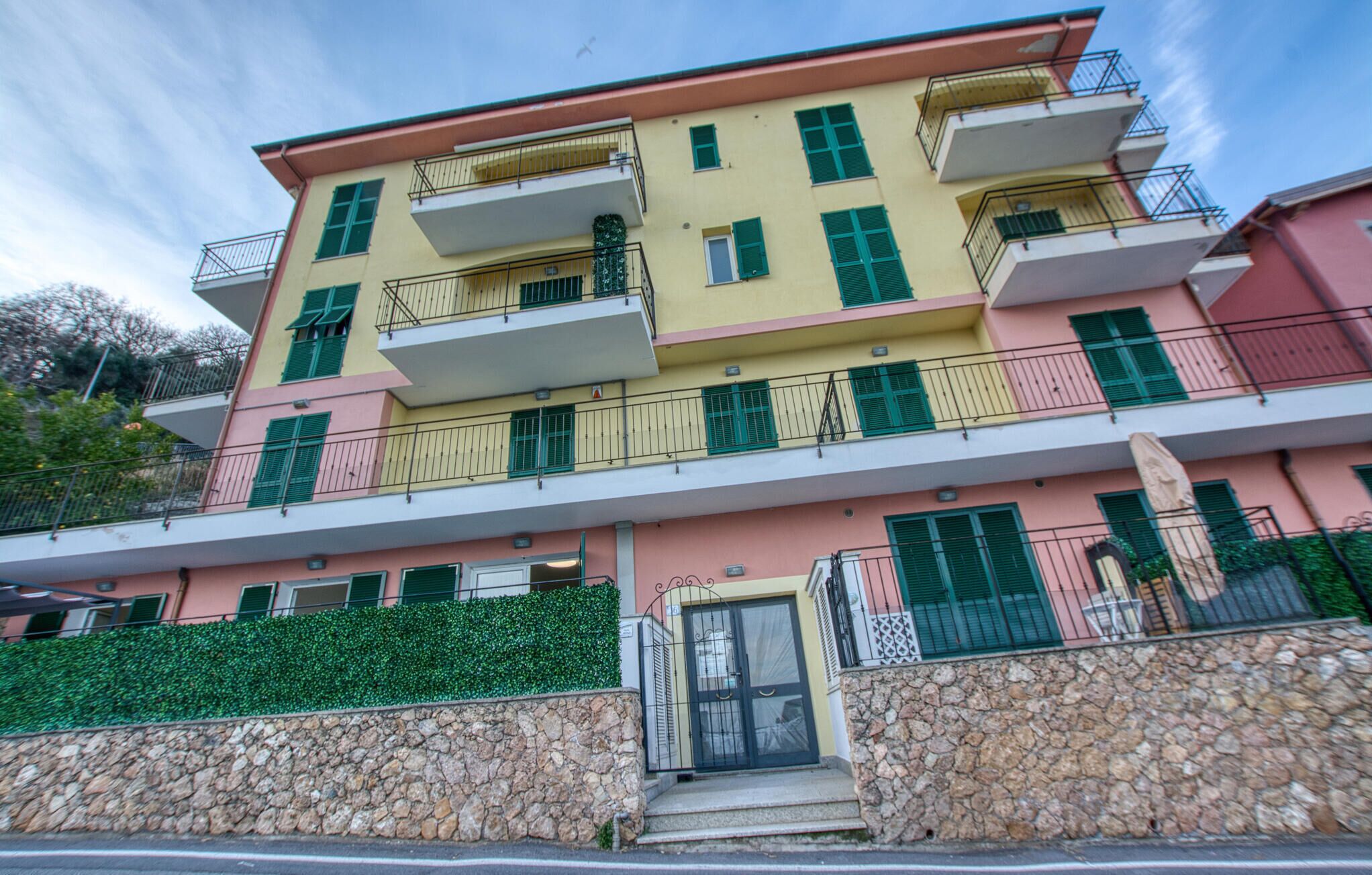 A multi-story building with balconies, a stone facade, and a door with a metal gate.