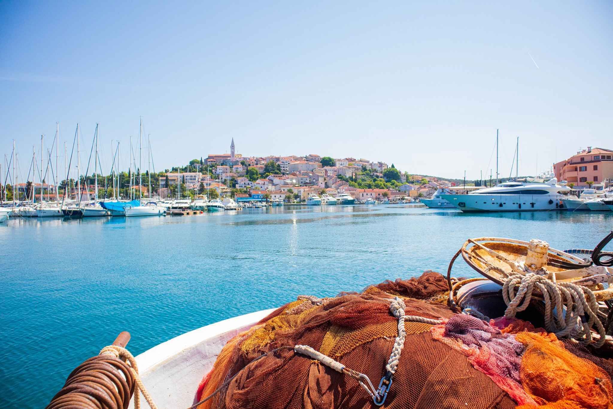 A marina with boats docked, a town in the background, and a hill with a tower.