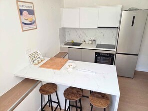 A modern kitchen with a marble countertop, a sink, a stove, and a refrigerator. There are three stools at the island. - Holiday apartment near the beach (Tkon)