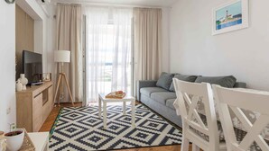 Un soggiorno moderno con un divano grigio, una poltrona bianca, un tavolino con un vassoio e una TV su un mobile in legno.