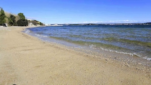 Una spiaggia con acque cristalline, un litorale di ciottoli e edifici in lontananza.