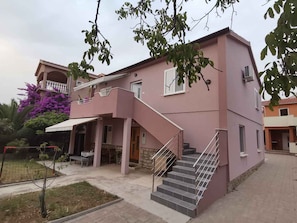 A two-story building with a pink exterior, a balcony, and a staircase leading to the upper floor. - Holiday apartment with balcony and air conditioning (Biograd na Moru)