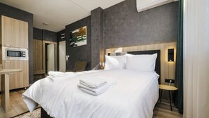 Moderni hotellihuone, jossa on suuri sänky, työpöytä, jossa on mikroaaltouuni, tuoli ja pieni pöytä.