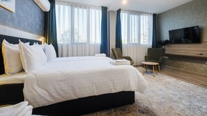 A modern hotel room with a large bed, a flat-screen TV, a seating area with chairs, and a large window with curtains. - А17 Plovdiv Apartments Next to Rowing Channel app3 (Plovdiv)