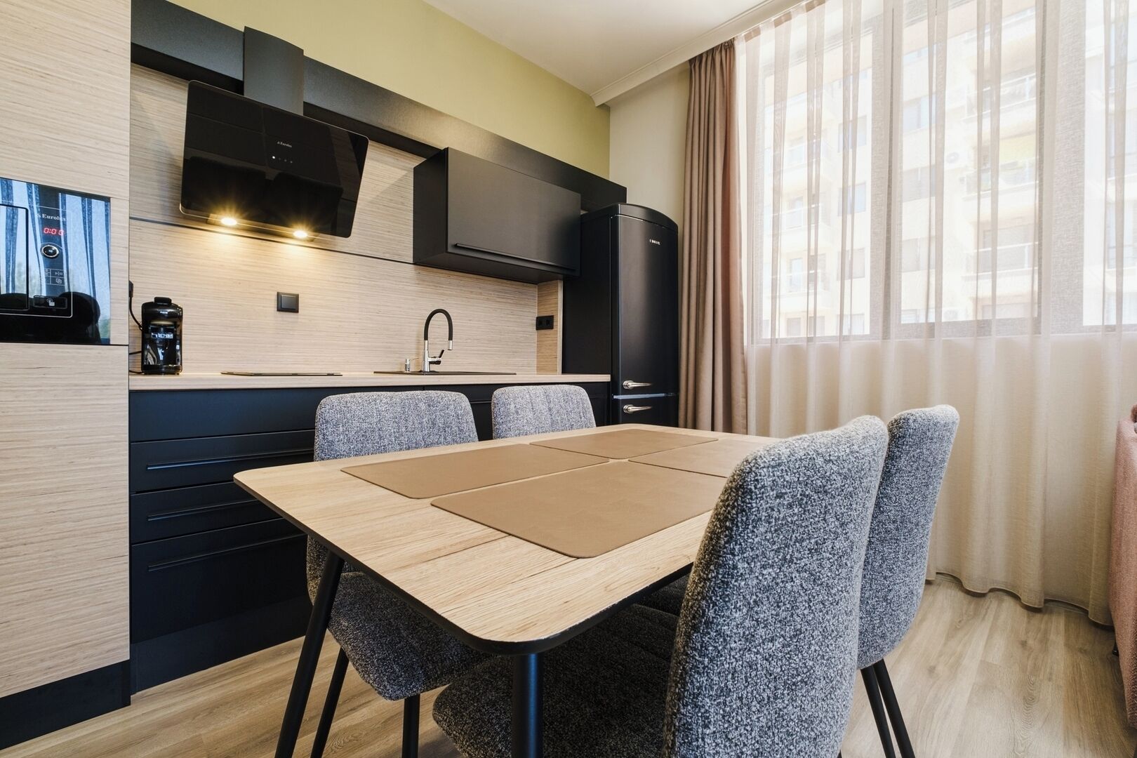 Een moderne keuken met een eettafel en stoelen, een inbouwoven en een koelkast.
