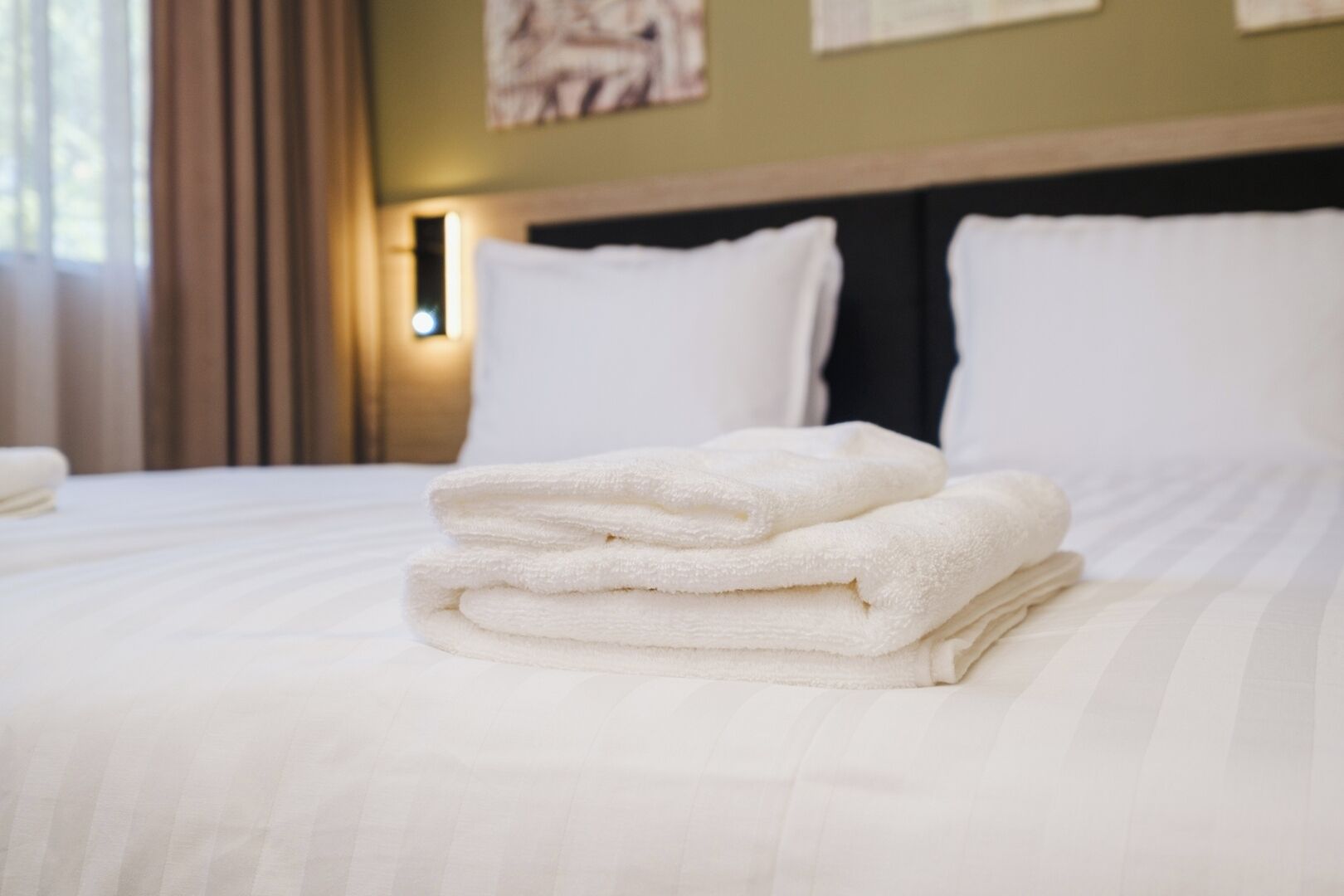 A neatly made bed with folded white towels and a headboard with wall-mounted lights.
