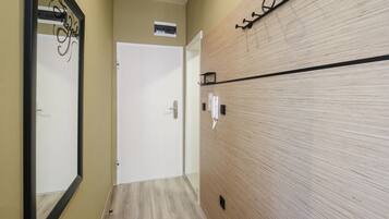 A hallway with a wooden floor, a white door, a wall-mounted telephone, and a mirror with a decorative frame.