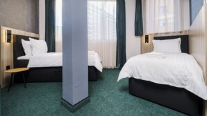 Habitación de hotel con dos camas, un pilar grande y vistas a edificios a través de las ventanas.