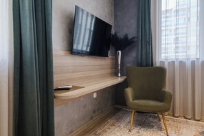 A modern living room with a flat-screen TV mounted on a wooden wall, a green armchair, and a decorative vase. - А17 Plovdiv Apartments Next to RowingChannel app16 (Plovdiv)