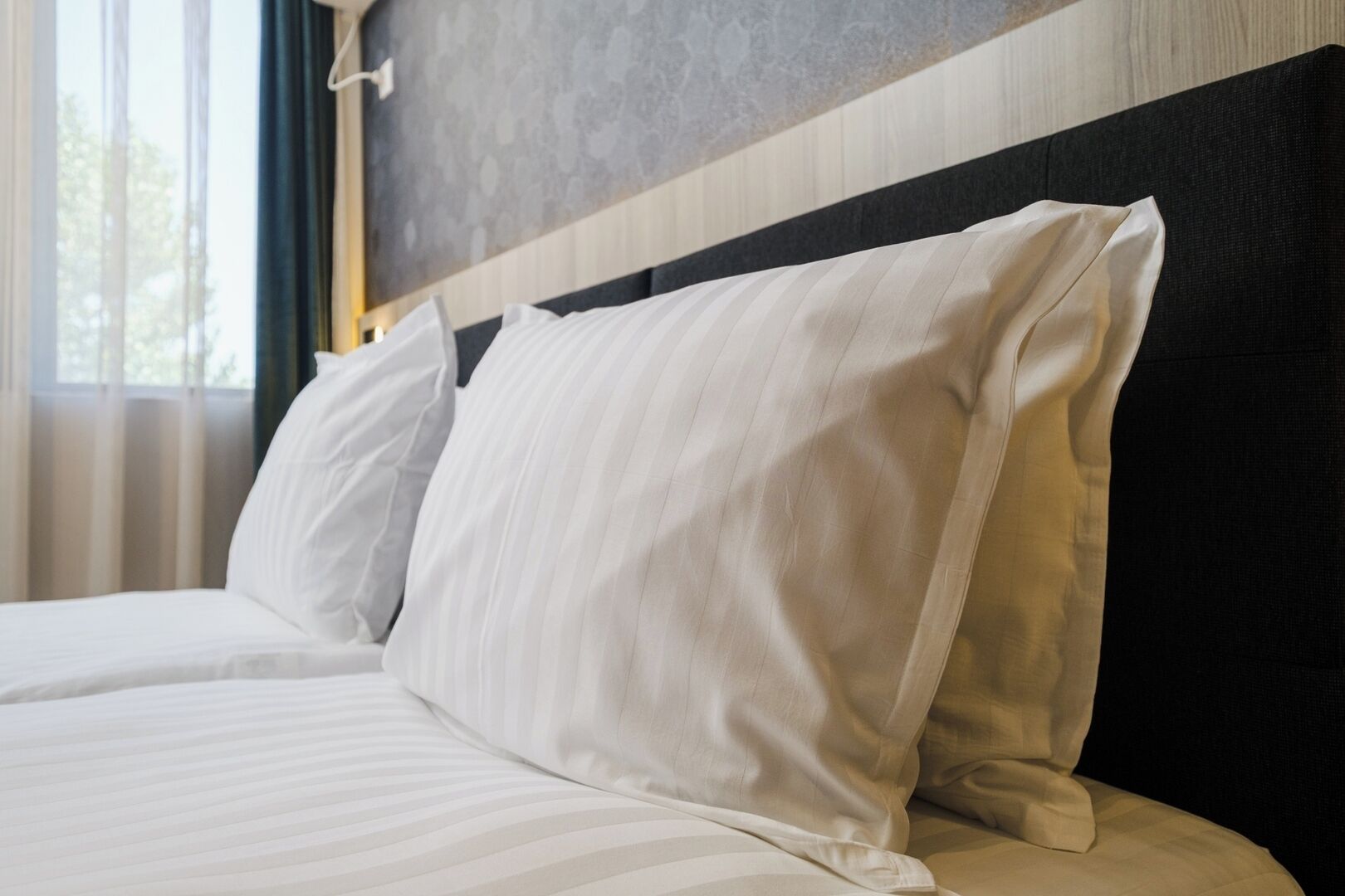 A neatly made bed with white linens and a dark headboard.