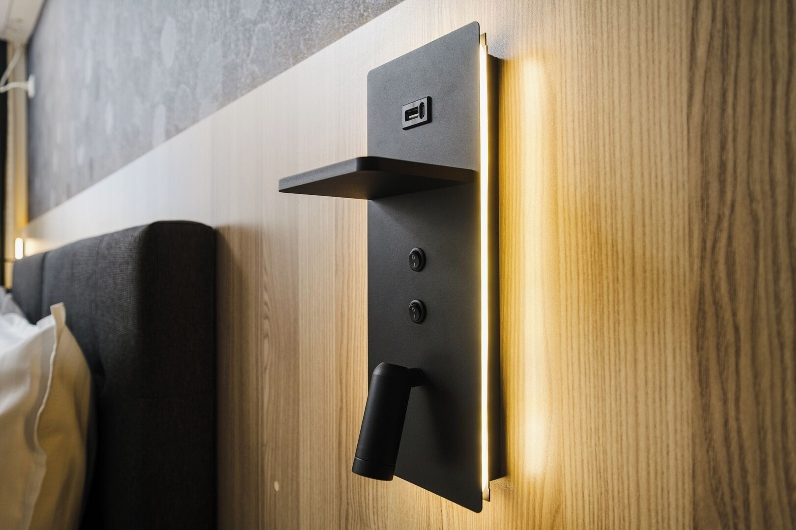 A wall-mounted light switch and outlet on a wooden panel, with a black fabric-covered object to the left.
