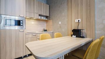 A modern kitchen with wooden cabinets, a built-in microwave, and a dining area with a curved table and yellow chairs.