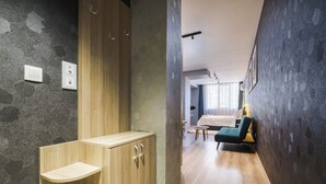 A modern hotel room with a wooden wardrobe, a small bedside table, a green sofa, and a large window with curtains.