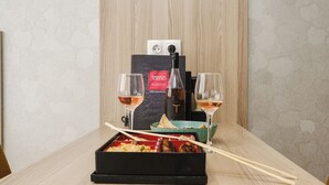 Une table dressée avec une boîte de sushis, deux verres de vin et une bouteille de vin, le tout posé sur une table en bois devant un mur à texture.