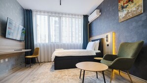 Quarto de hotel com cama, duas cadeiras, uma mesinha, televisão e ar condicionado.