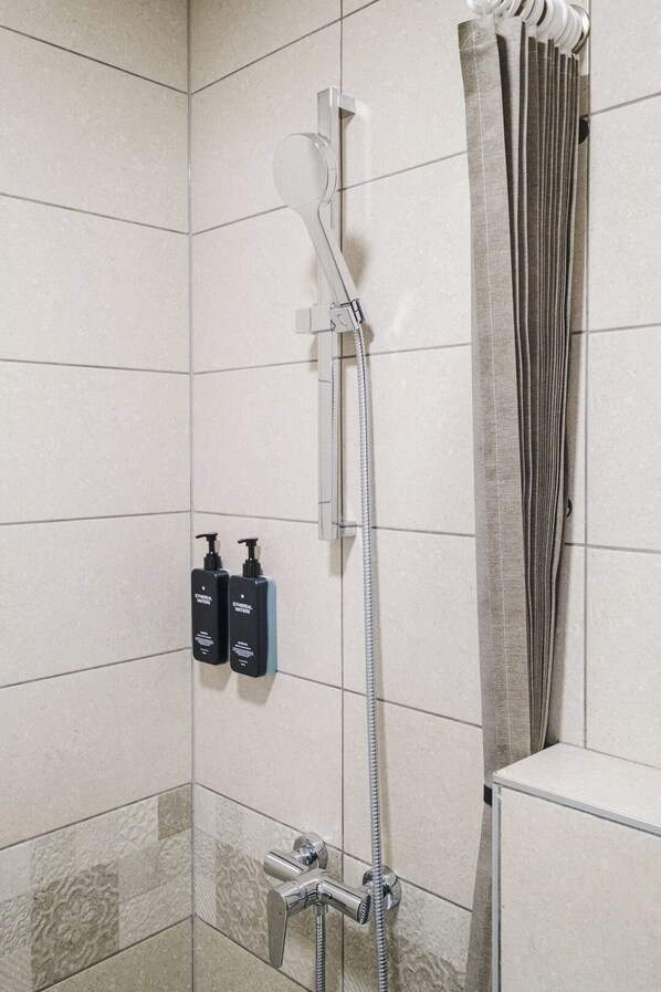 Une salle de bain avec une douche, des murs carrelés et deux bouteilles de shampoing.