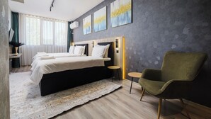Une chambre d’hôtel moderne avec deux lits, une grande fenêtre avec des rideaux, un fauteuil vert et des œuvres d’art accrochées au mur.