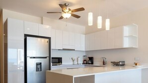 A modern kitchen with white cabinetry, a stainless steel refrigerator, a built-in oven, a microwave, a coffee maker, and pendant lighting. - Ocean Heaven: New Downtown Condo (Isla Mujeres)